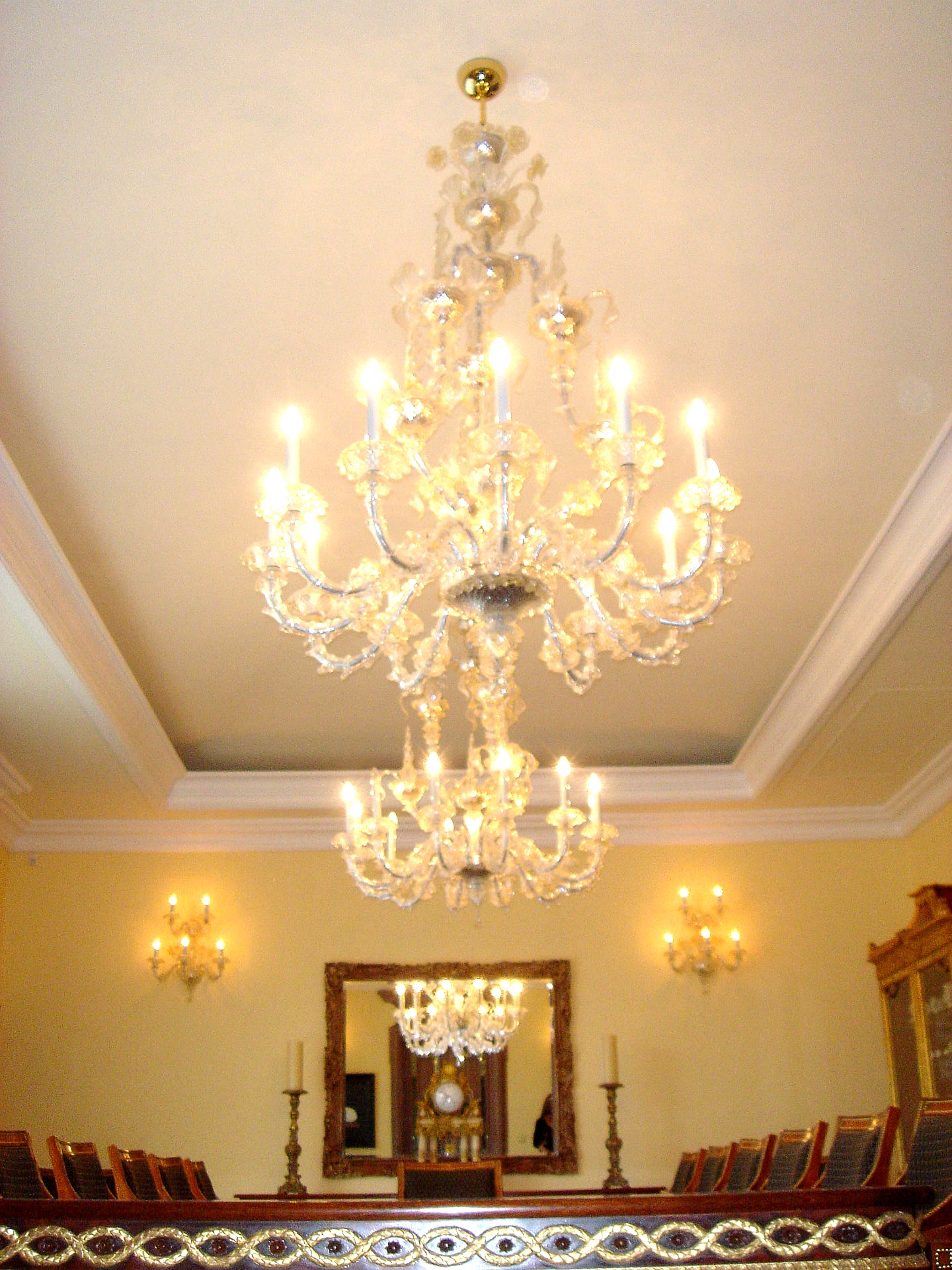 Formal dining room beneath a two-tier crystal chandelier with matching wall sconces