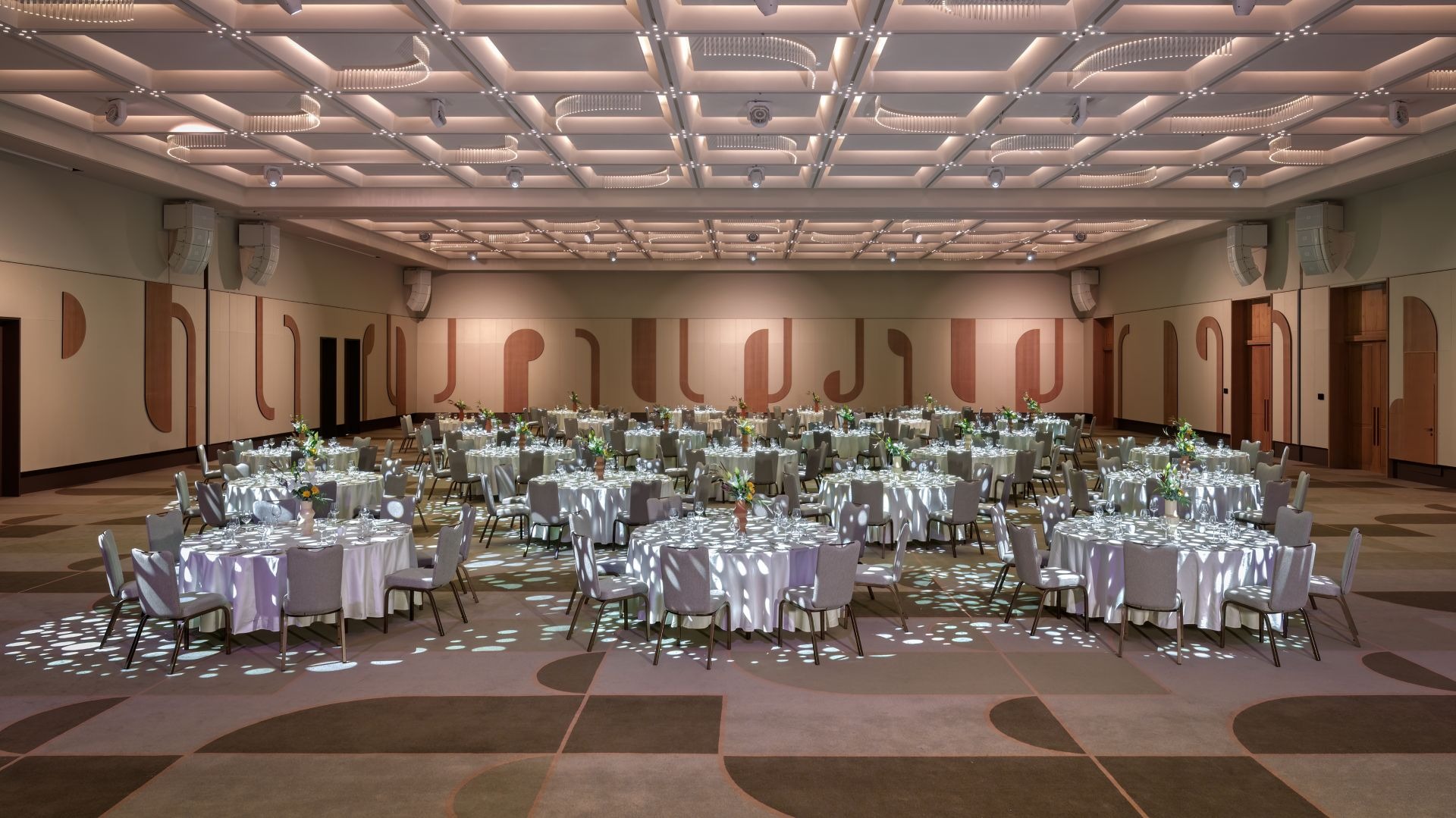 Ballroom set for a banquet with round tables beneath the illuminated coffered ceiling