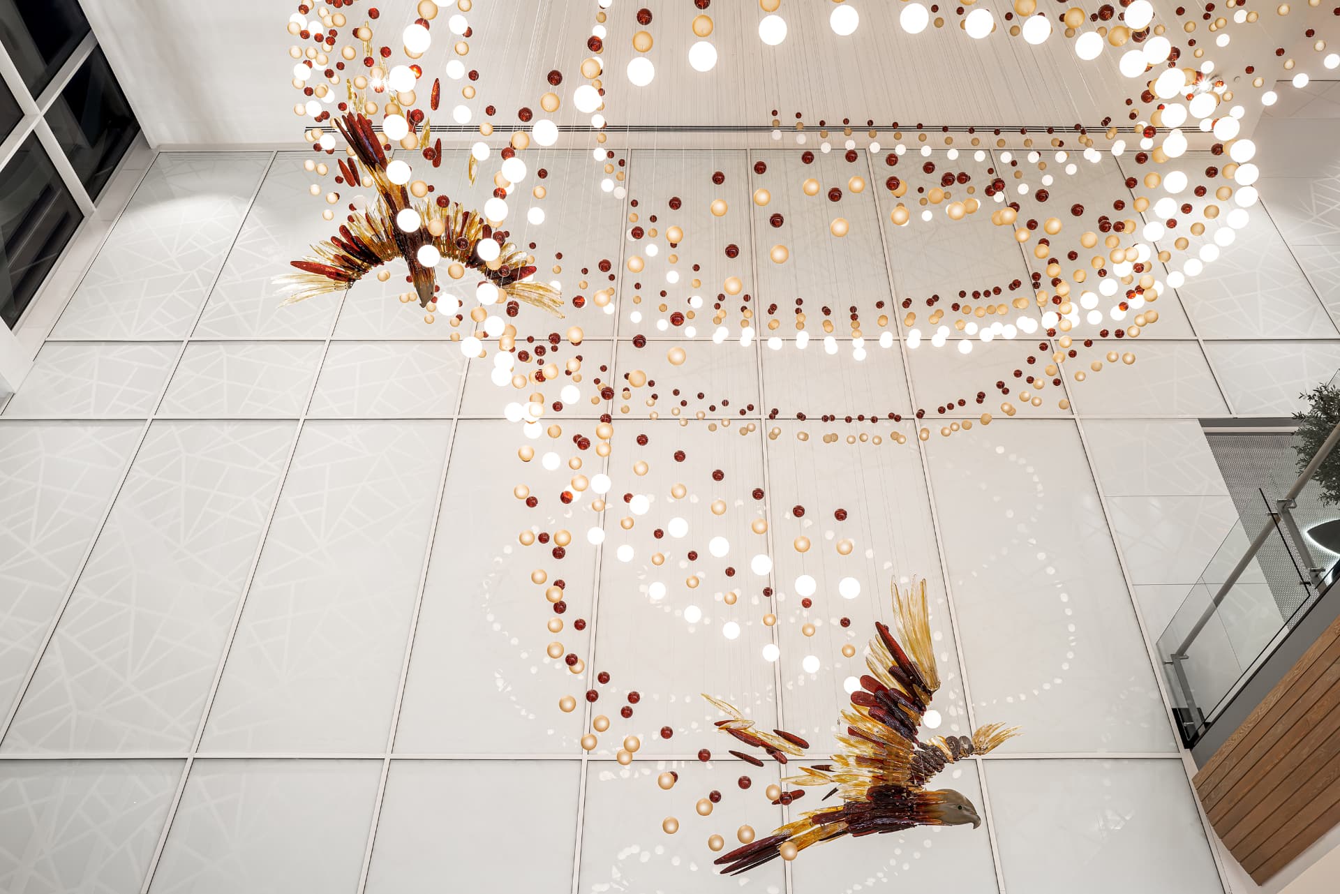 Two glass birds suspended within the illuminated ceiling composition